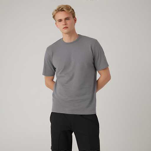 A young man is standing against a plain white background wearing a gray t-shirt and black shorts with his hands tucked into his pockets.